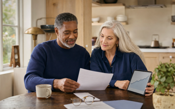A mixed-race couple in their early 60s calmly reviewing a one-page retirement summary at their kitchen table